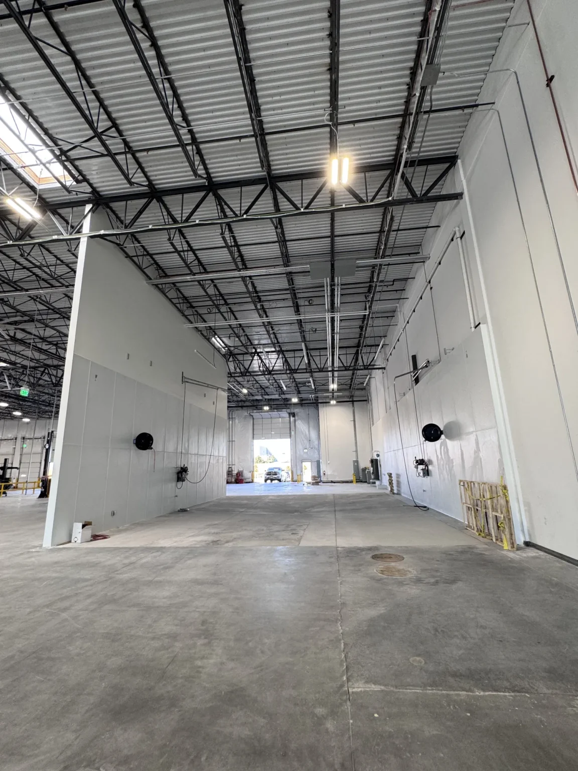 commercial-11 Large empty warehouse with high ceilings, exposed beams, and white walls, lit by overhead lights.