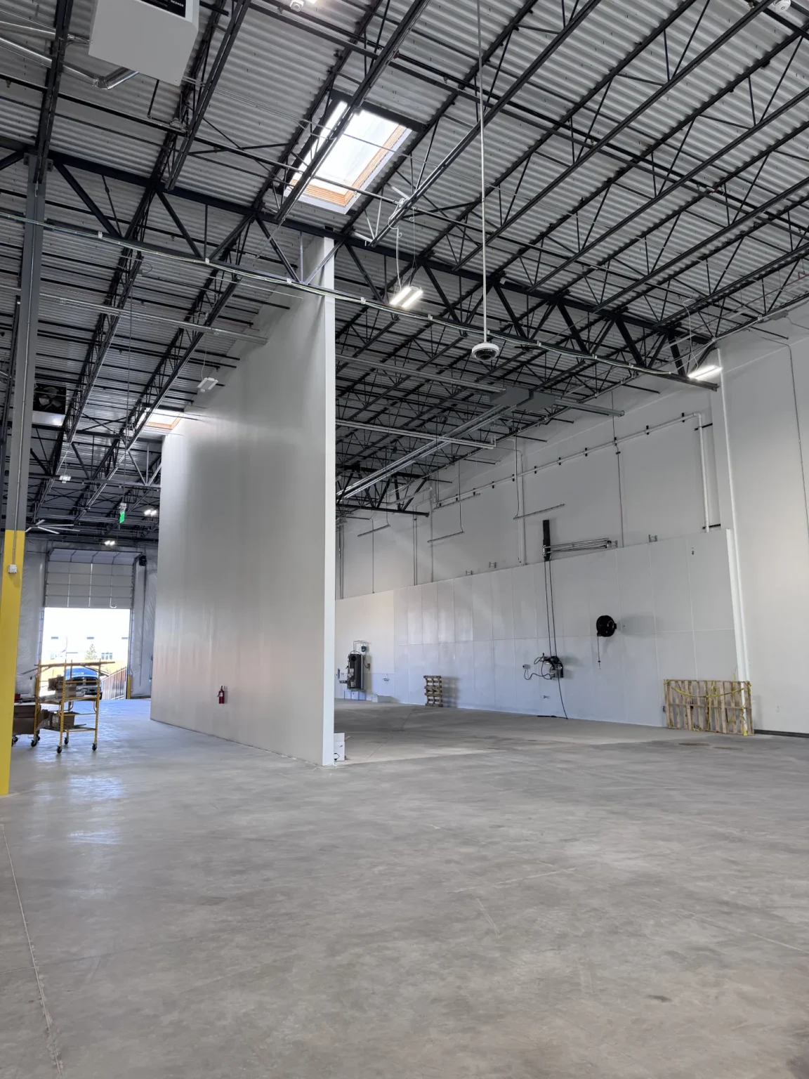 commercial-12 Spacious, empty warehouse with high ceilings, exposed beams, and white walls, lit by natural and artificial light.