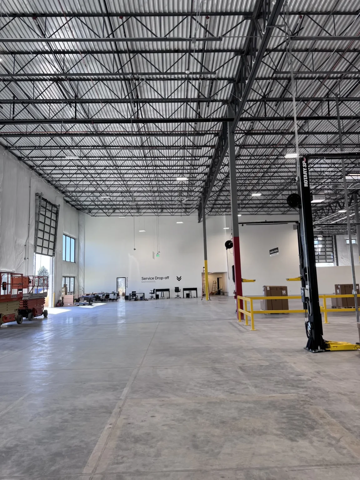 commercial-13 Large, empty warehouse with high ceilings, concrete floor, and some equipment and boxes near the walls.