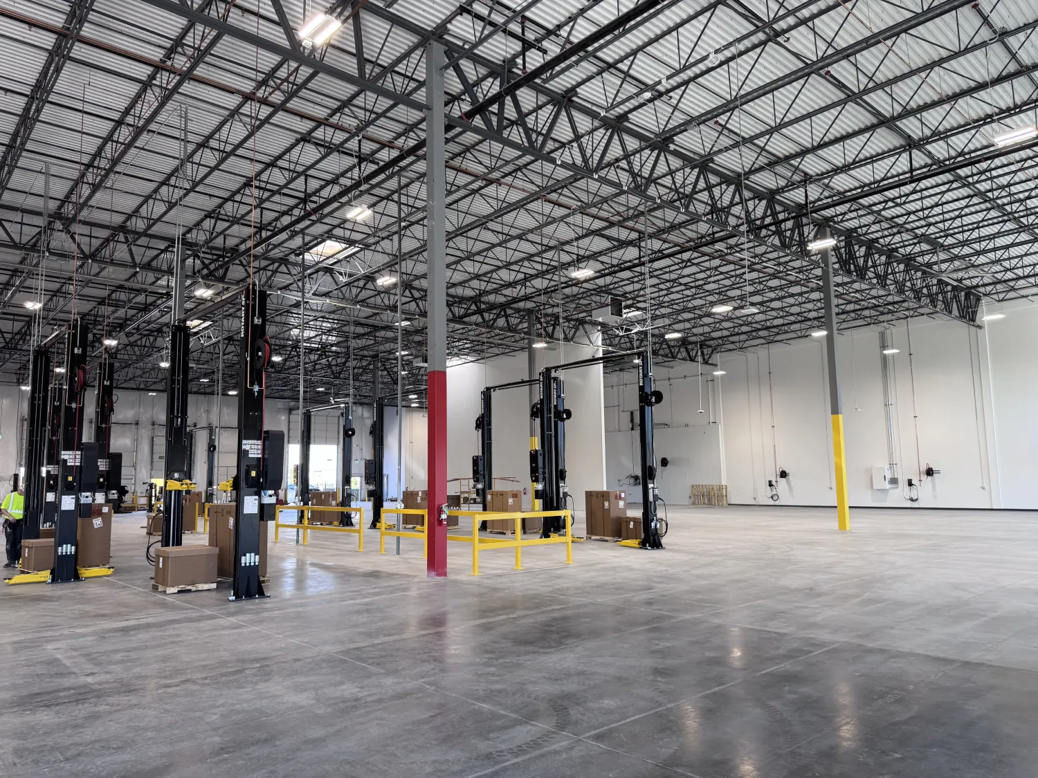 commercial-14 Large, empty warehouse interior with tall ceilings, lifts, boxes, and yellow safety barriers visible.