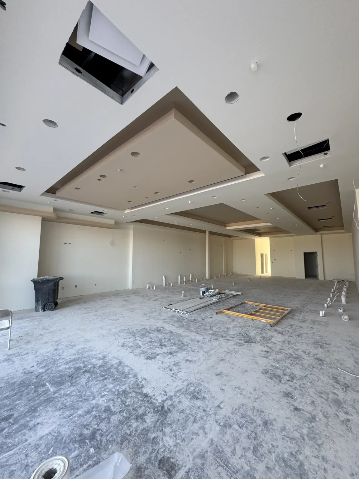 commercial-22 Large unfinished room with construction materials, recessed ceiling, and scattered debris on the floor.