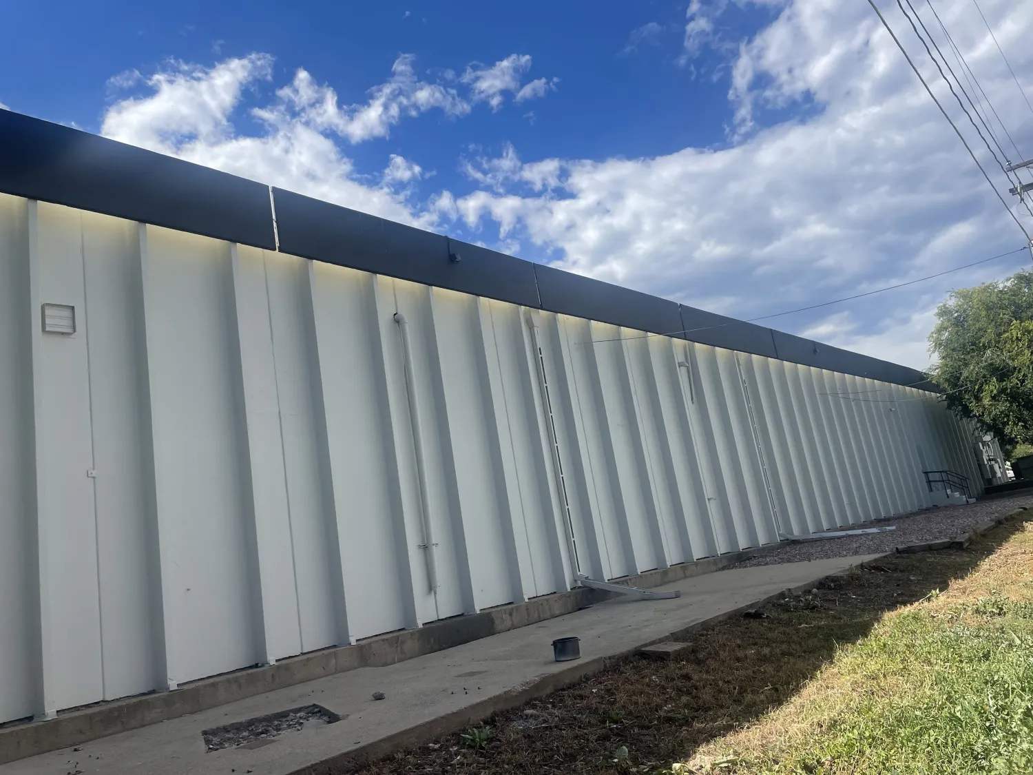 commercial-24 Long white industrial building with vertical siding, blue trim, sidewalk, grass, and a partly cloudy sky.