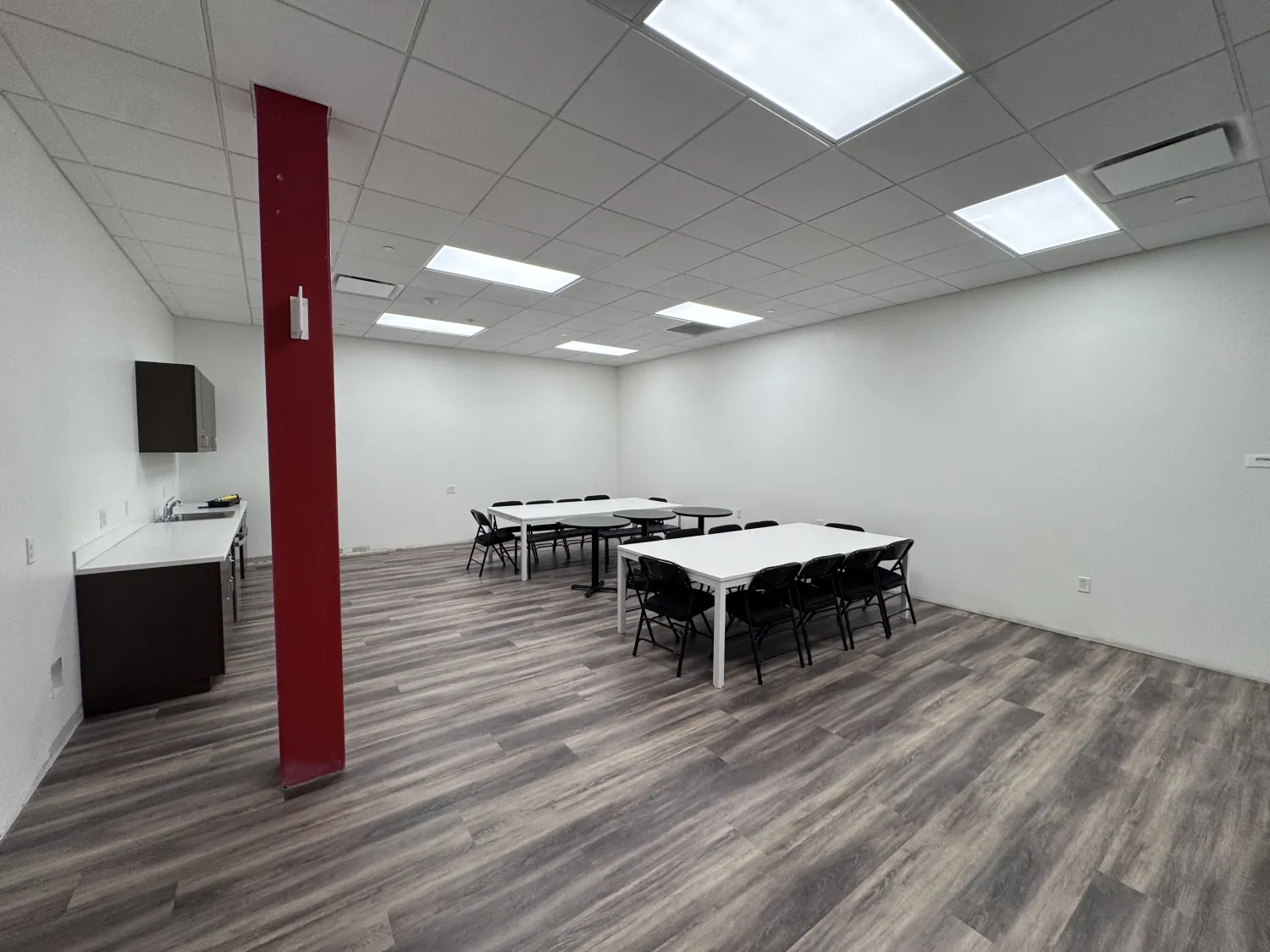 commercial-3 A modern, empty classroom with tables, chairs, bright lights, wood floors, and a red pillar.