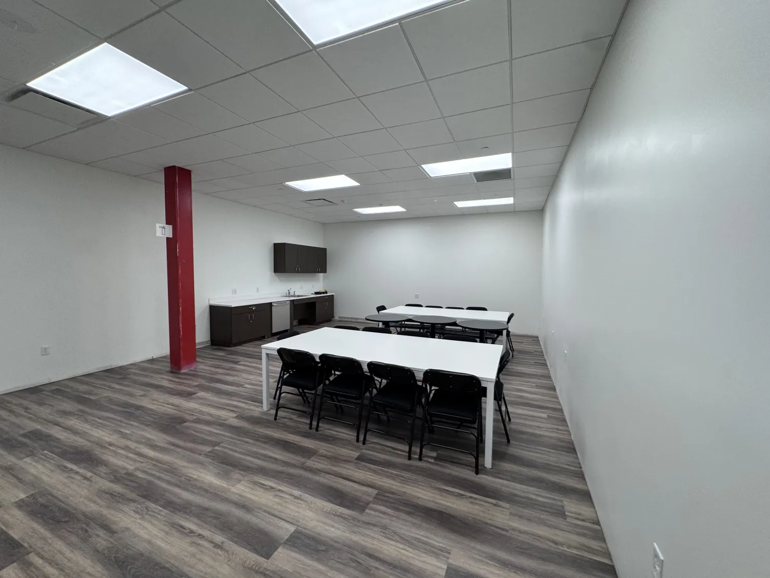 commercial-4 Empty room with folding chairs around tables, wood floors, white walls, cabinets, and a red pillar.