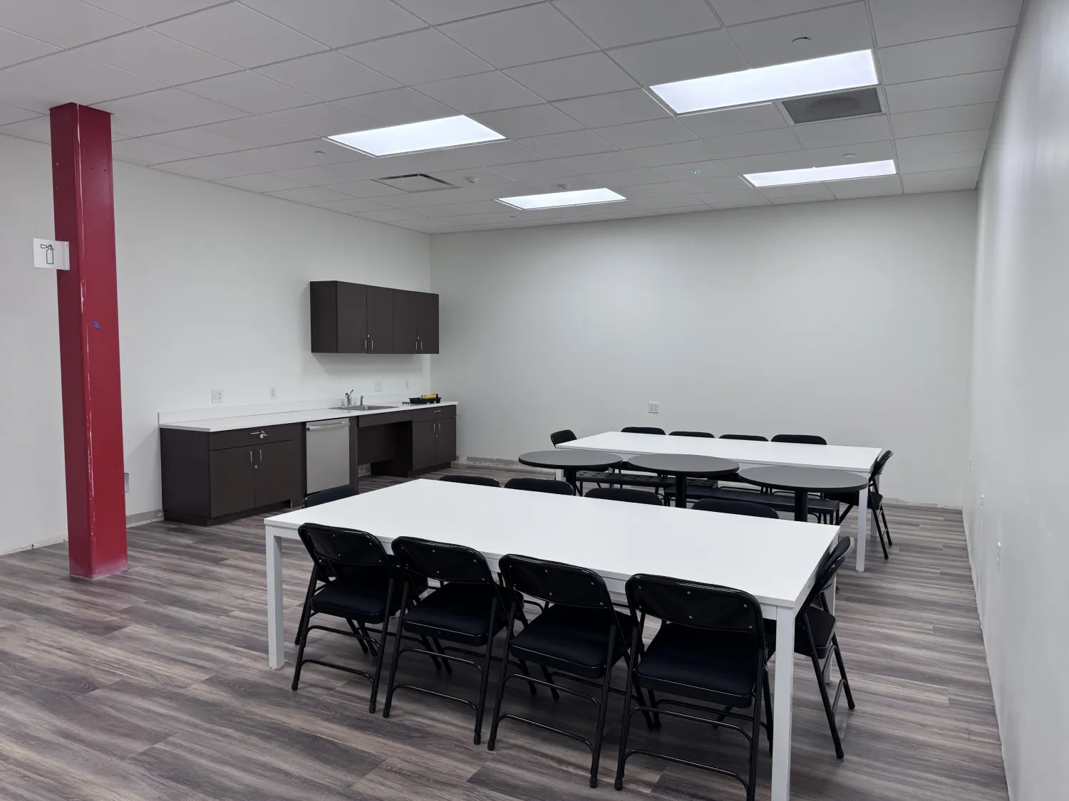 commercial-5 Breakroom with white tables, black chairs, kitchenette, wood flooring, and a red support column.
