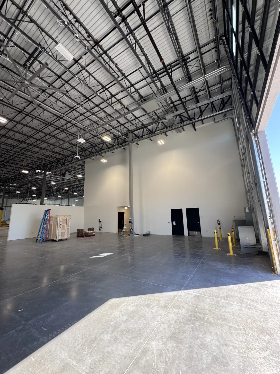 commercial-6 Spacious warehouse interior with high ceilings, exposed beams, crates, and equipment near a large open door.