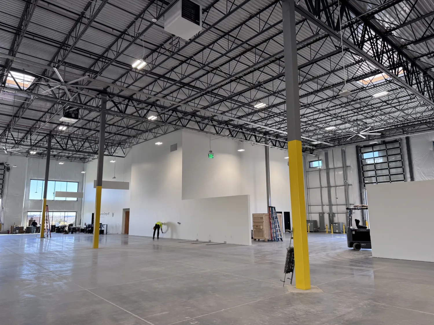 commercial-7 Large, mostly empty warehouse space with high ceilings and a few workers and equipment visible.