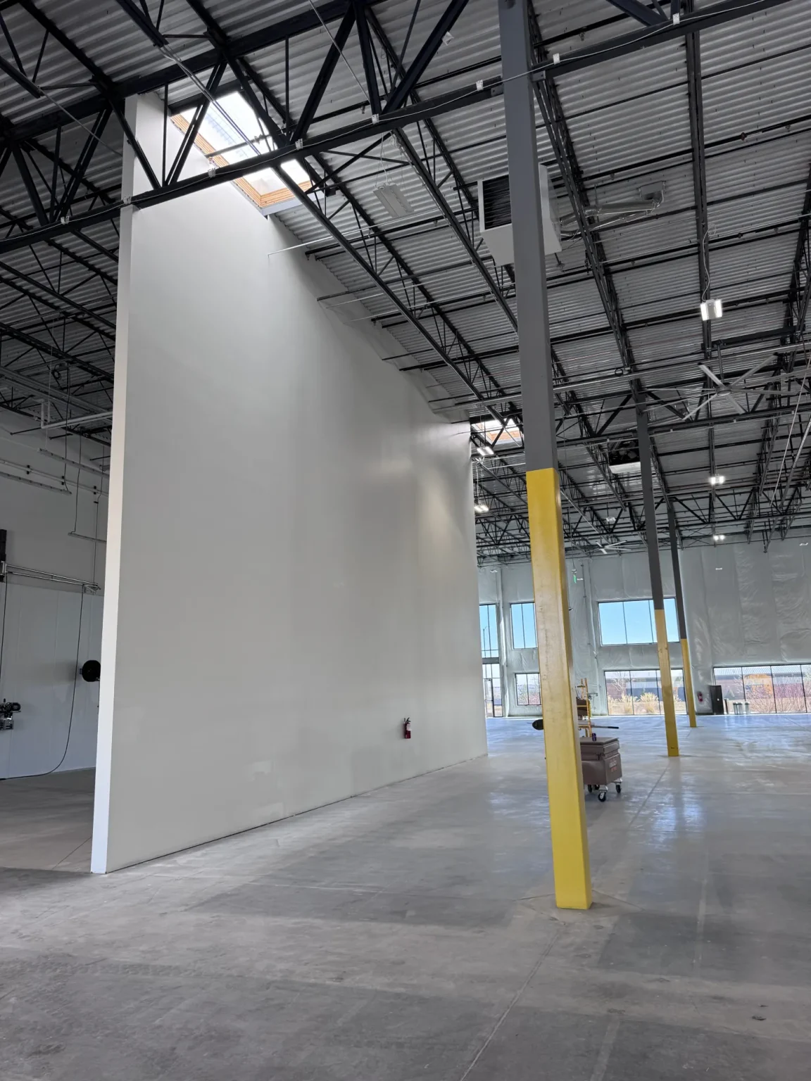 commercial-8 Large empty warehouse with high ceilings, a tall white wall, and yellow safety padding on a support beam.