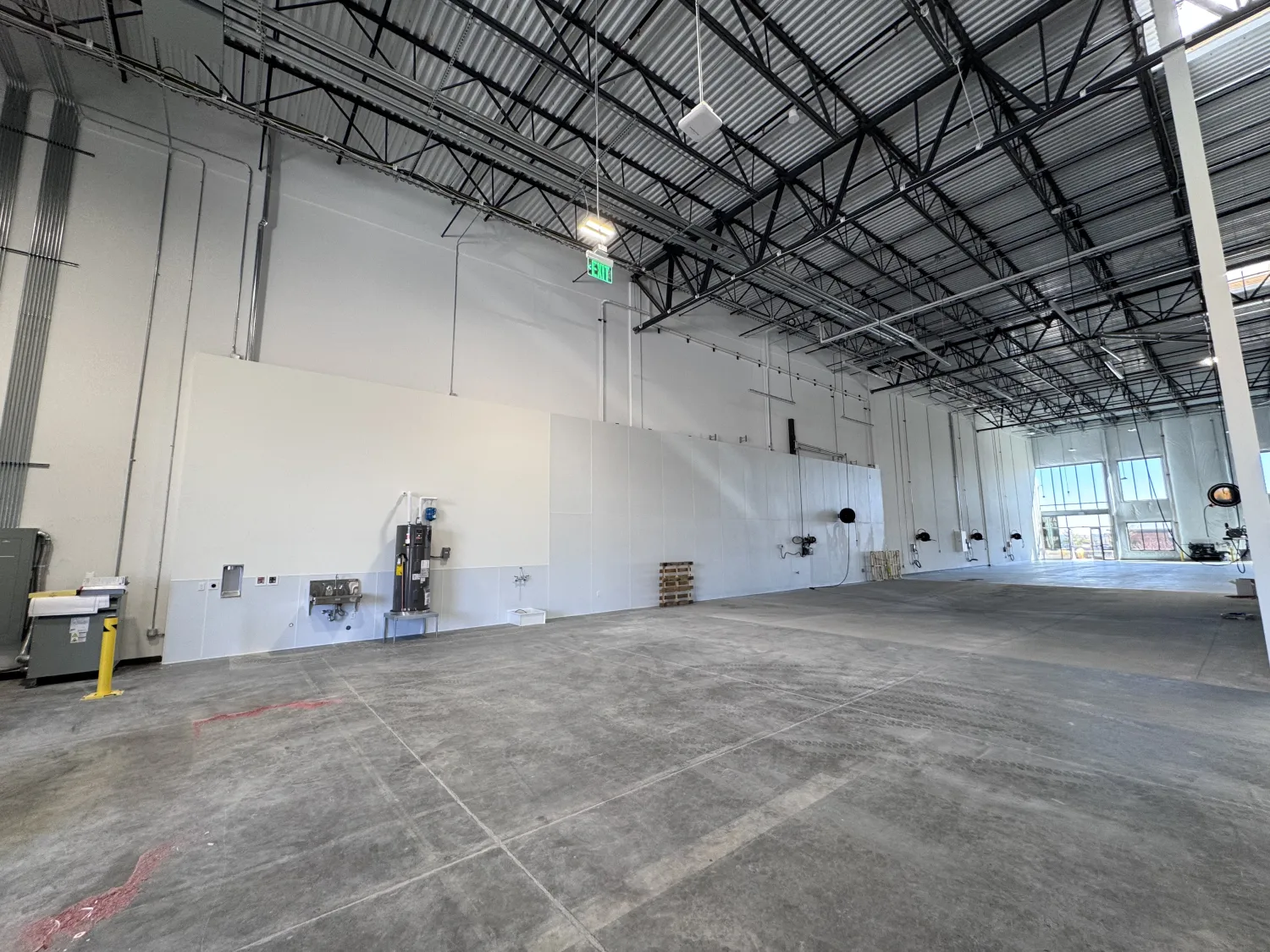 commercial-9 Spacious empty warehouse with high ceilings, exposed beams, large windows, and scattered equipment.