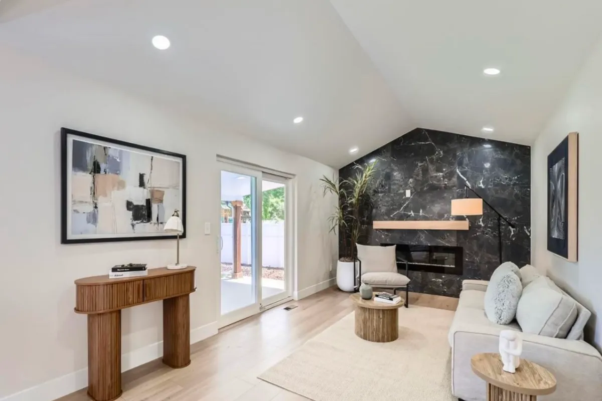 Modern living room with light walls, a marble accent wall, couch, abstract art, and sliding glass doors.