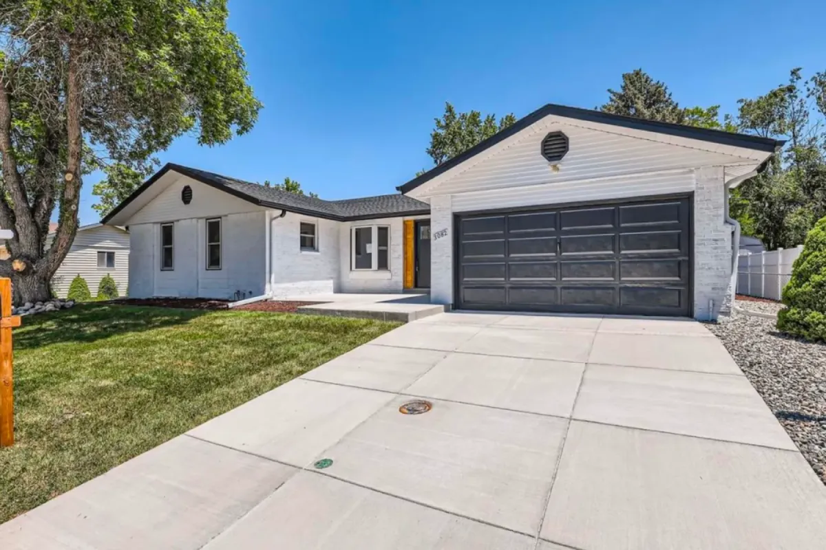 Modern white house with black garage door, wide driveway, green lawn, and clear blue sky.