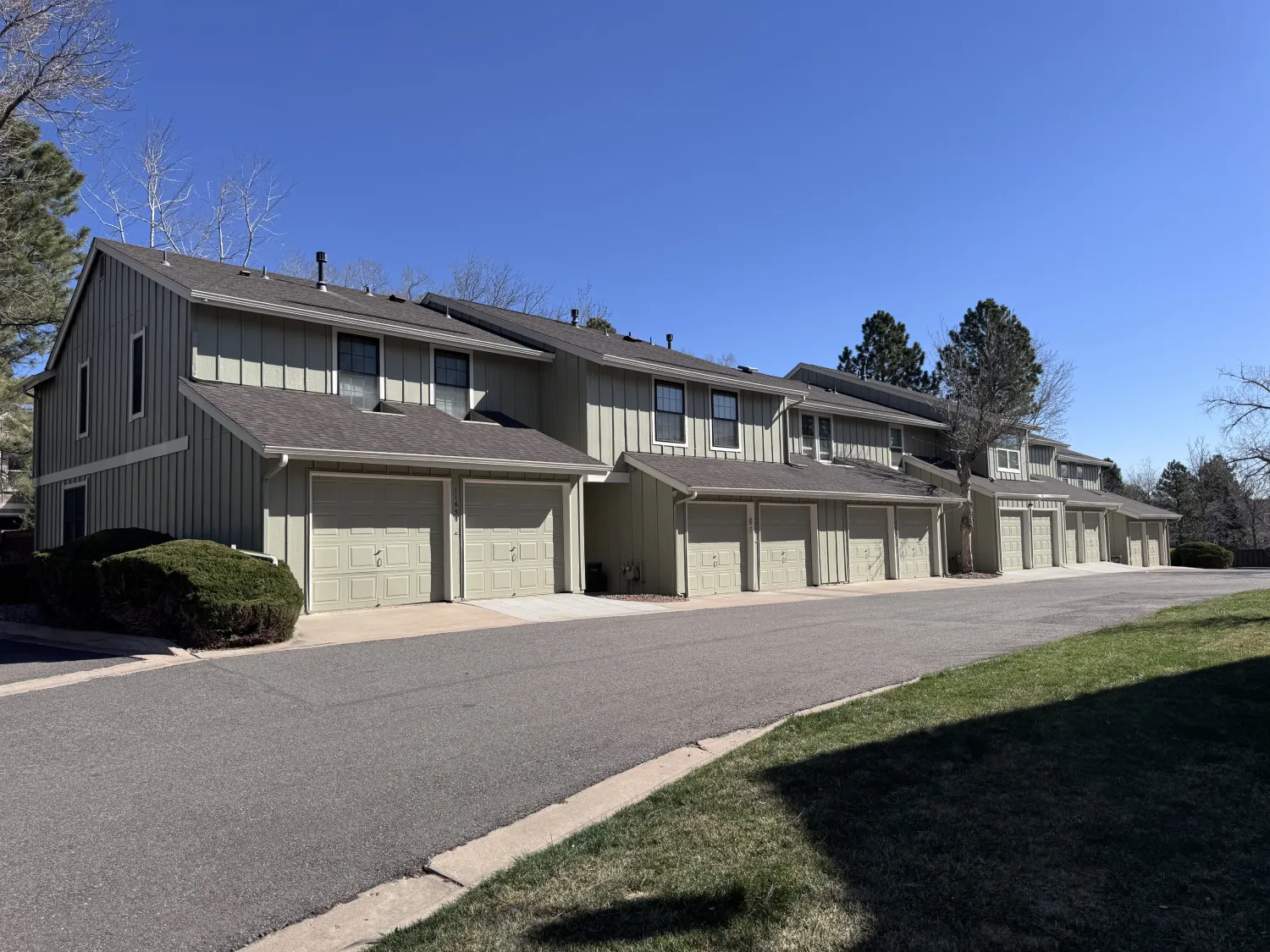 hoa-1 Row of tan townhouses with garages under a clear blue sky, trees in the background, grass in front.