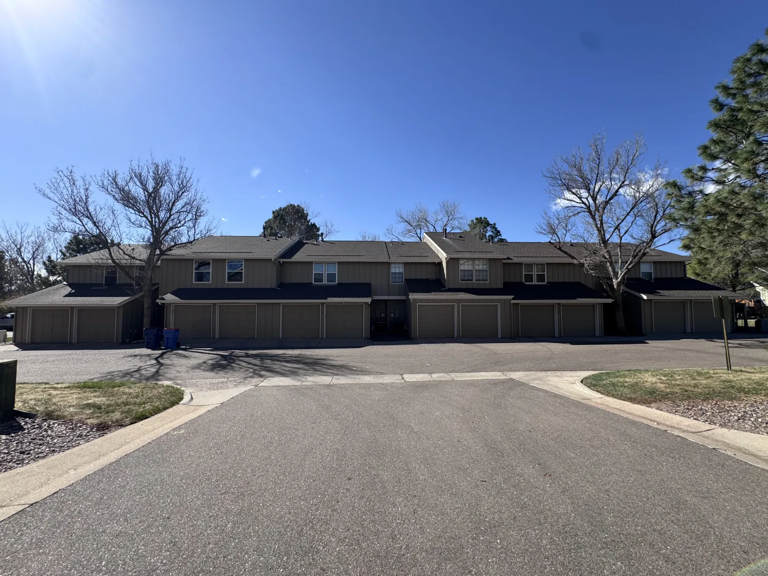 hoa-10 Two-story apartment building with garages, leafless trees, and clear blue sky on a sunny day.
