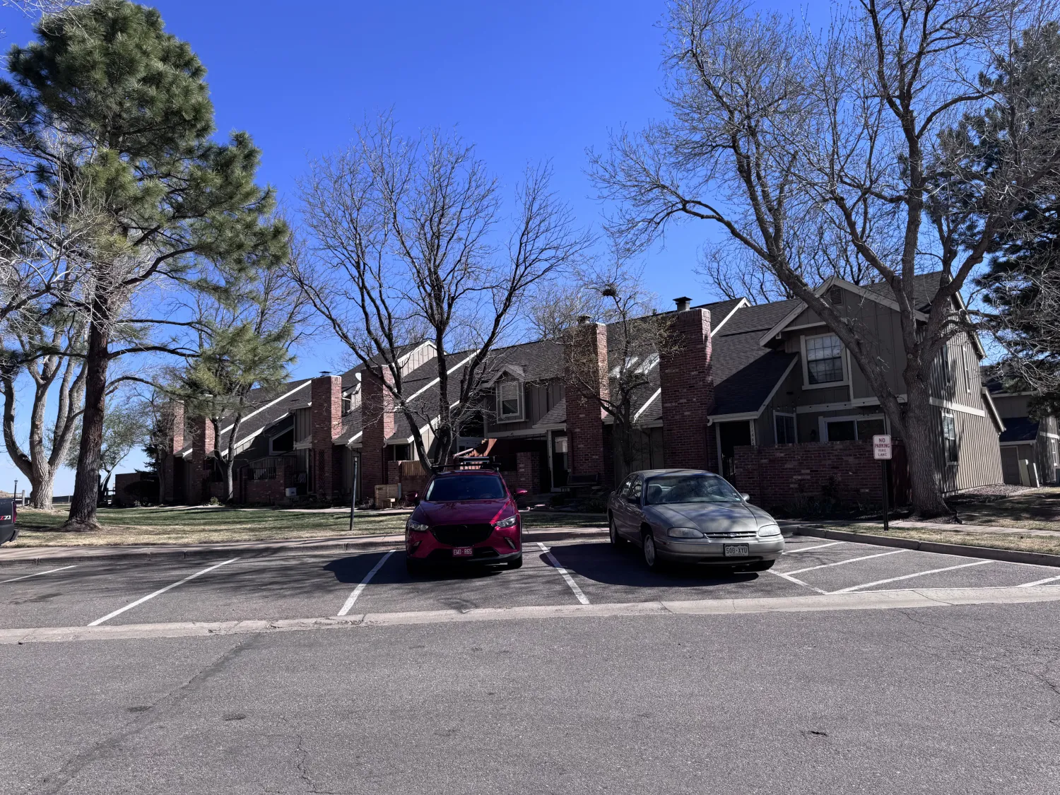 hoa-12 Two cars parked in front of a row of townhouses with bare trees on a sunny day.
