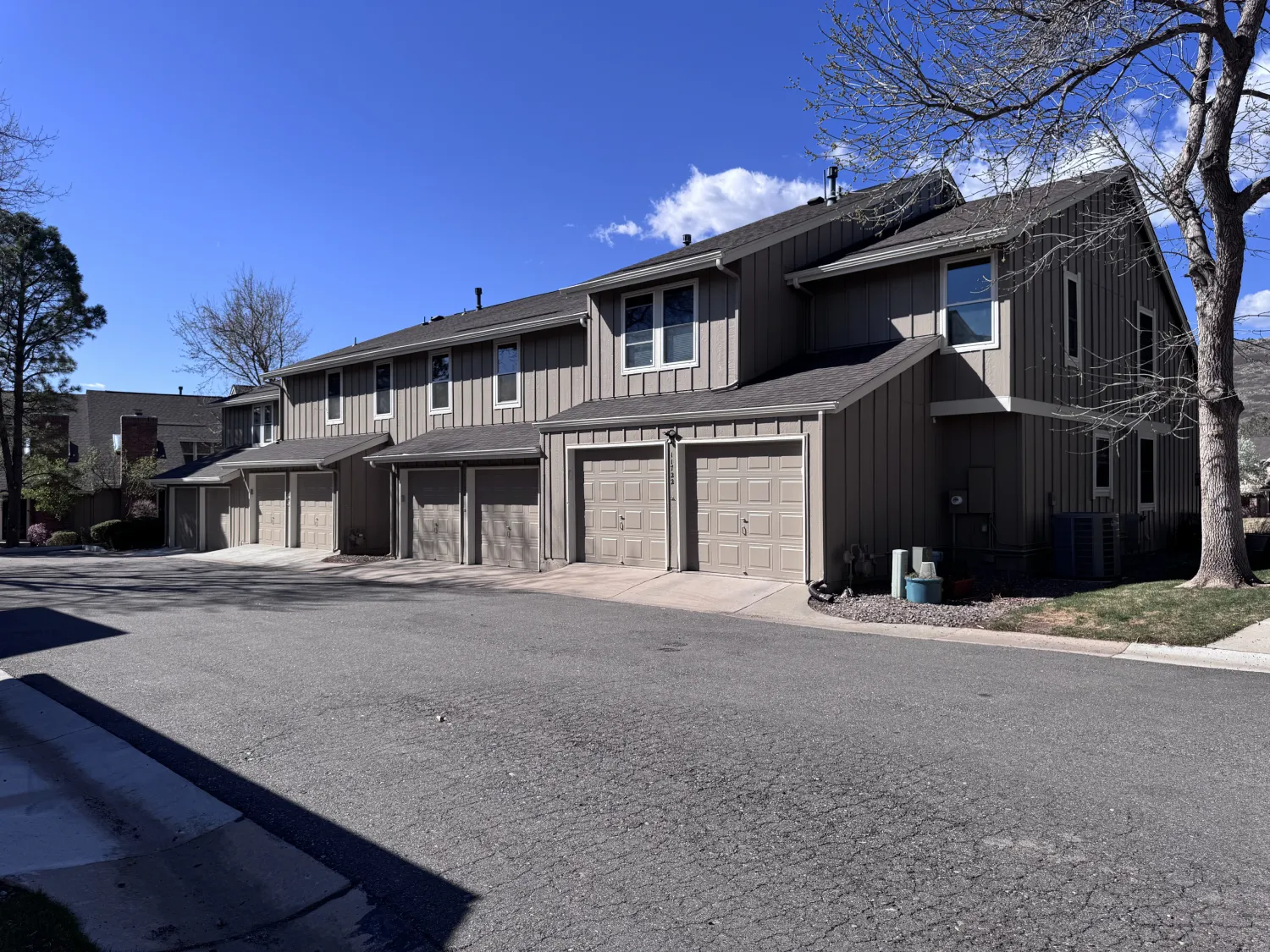 hoa-13 Row of modern beige townhouses with garages, leafless trees, and clear blue sky on a sunny day.