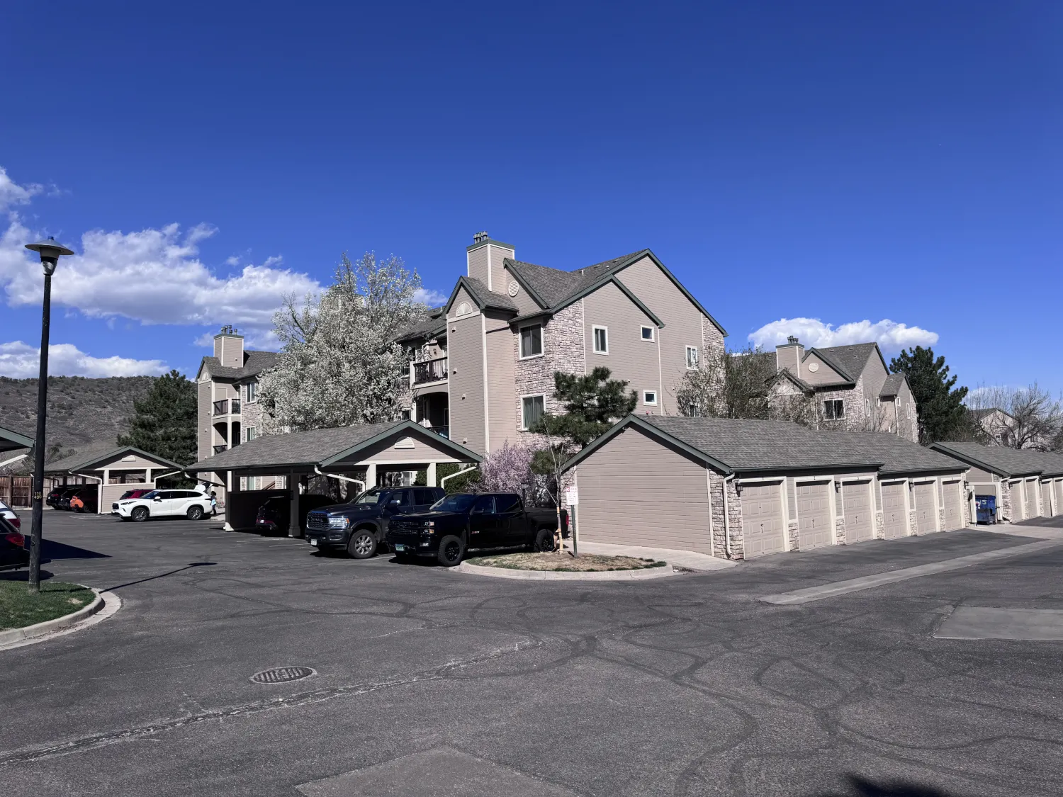 hoa-16 Apartment complex with garages and parked cars under a clear blue sky, trees in the background.