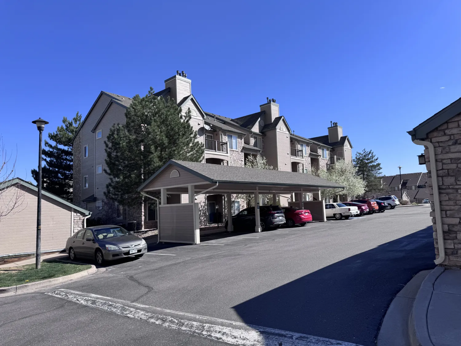 hoa-17 Three-story apartment building with covered parking and several cars under a clear blue sky.