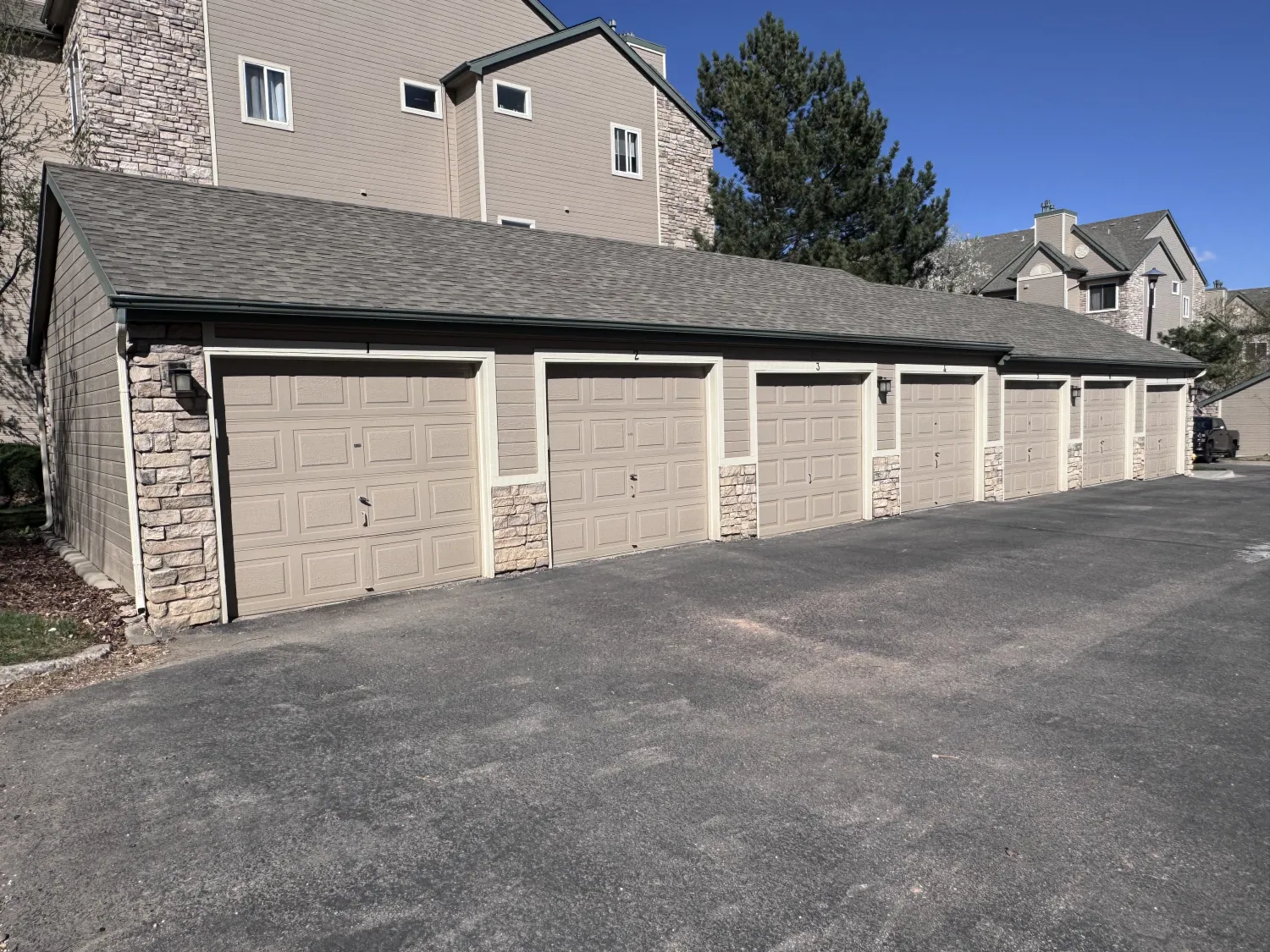 hoa-18 Row of beige garage doors with stone accents in front of an apartment building on a sunny day.
