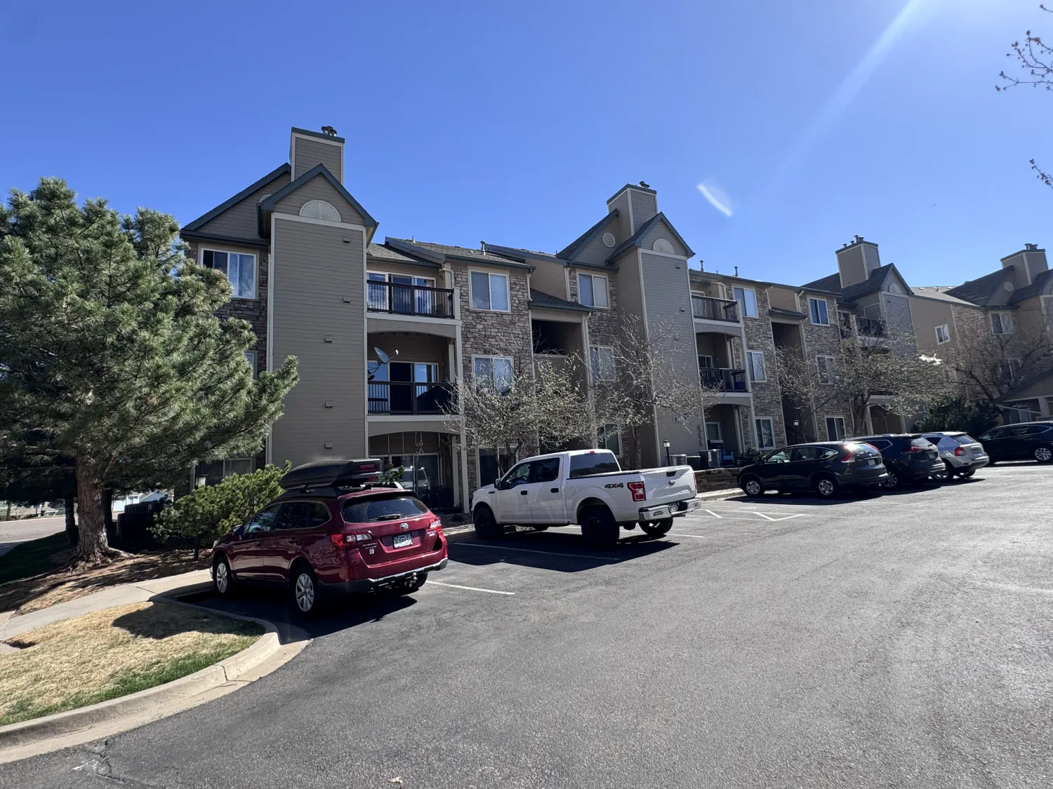 hoa-21 Apartment building with balconies and parked cars in a sunny parking lot.