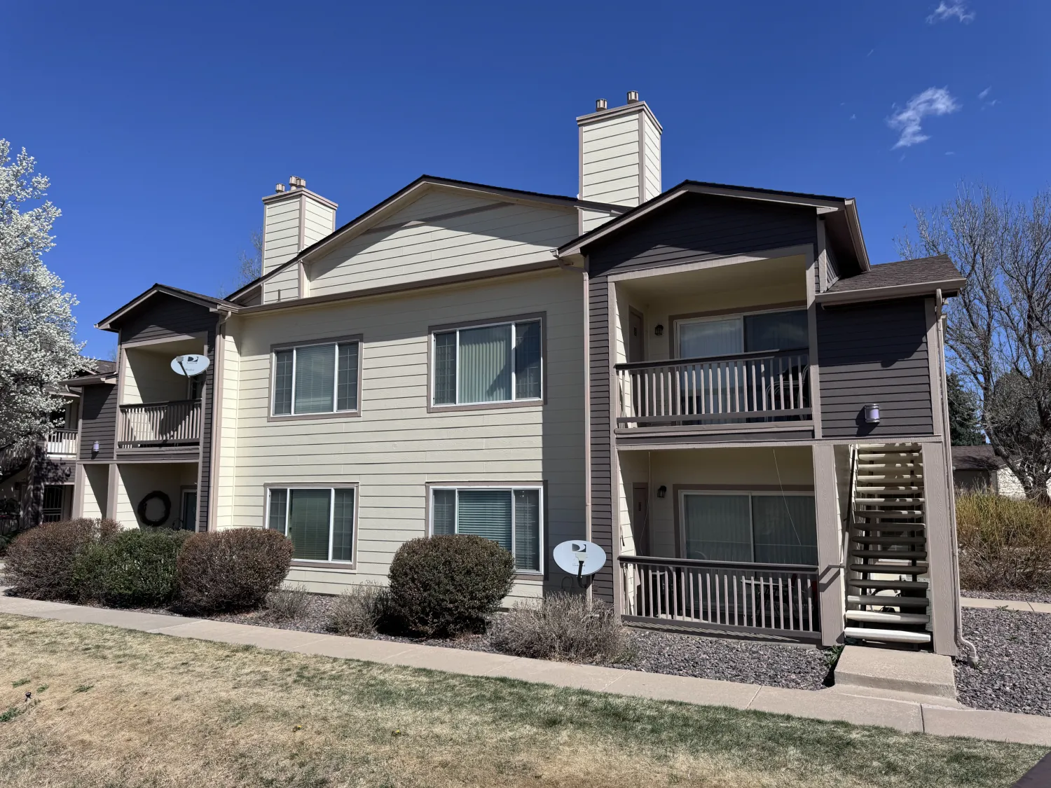 hoa-23 Two-story beige apartment building with balconies, satellite dishes, and a small lawn out front.