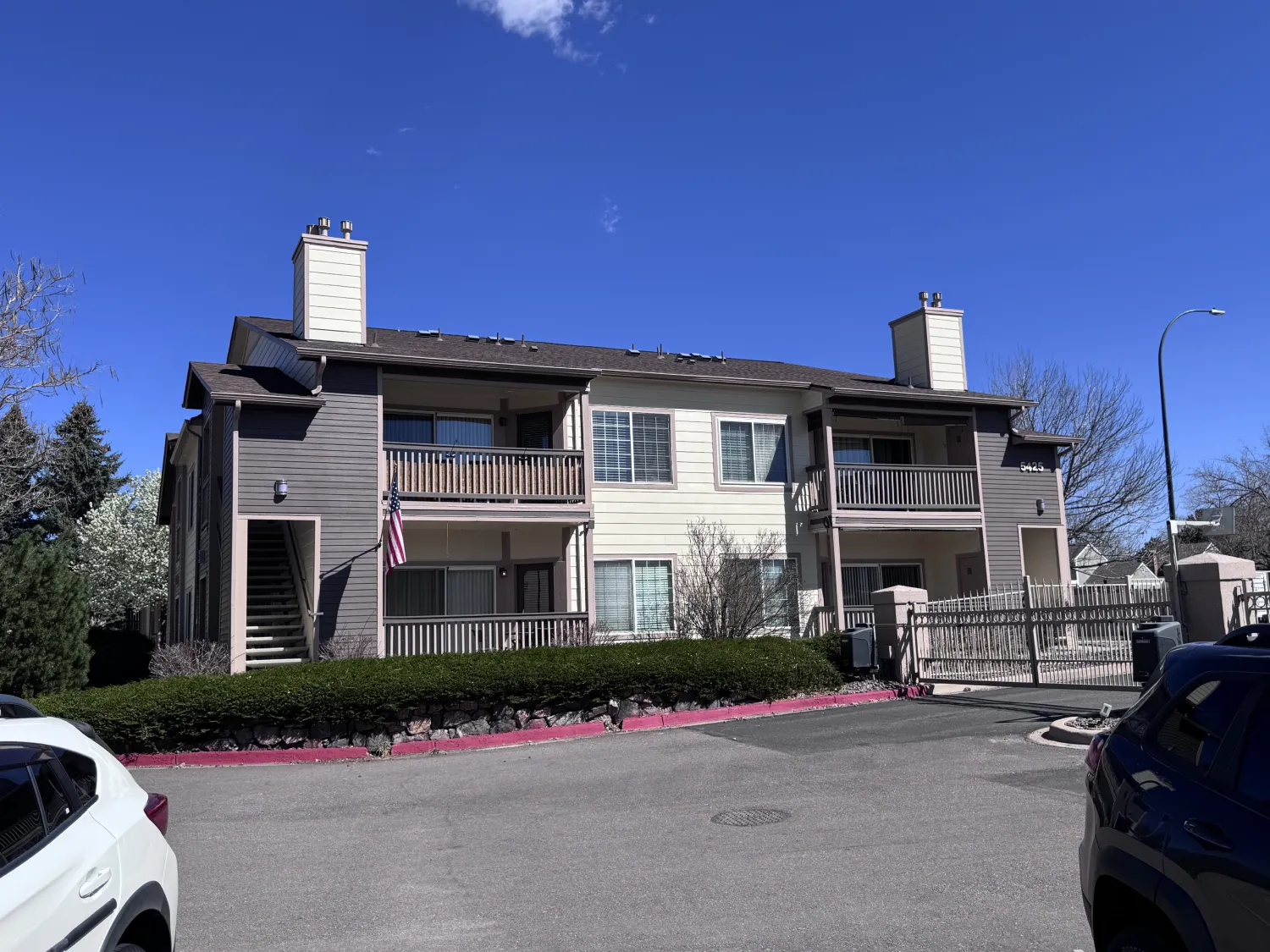 hoa-27 Two-story apartment building with balconies, cars parked in front, and a clear blue sky above.