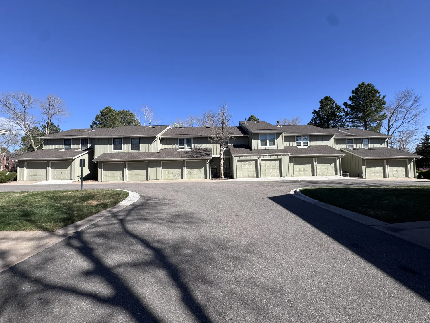 hoa-3 Row of townhouses with closed garages under a clear blue sky, trees in the background, and shadows on pavement.