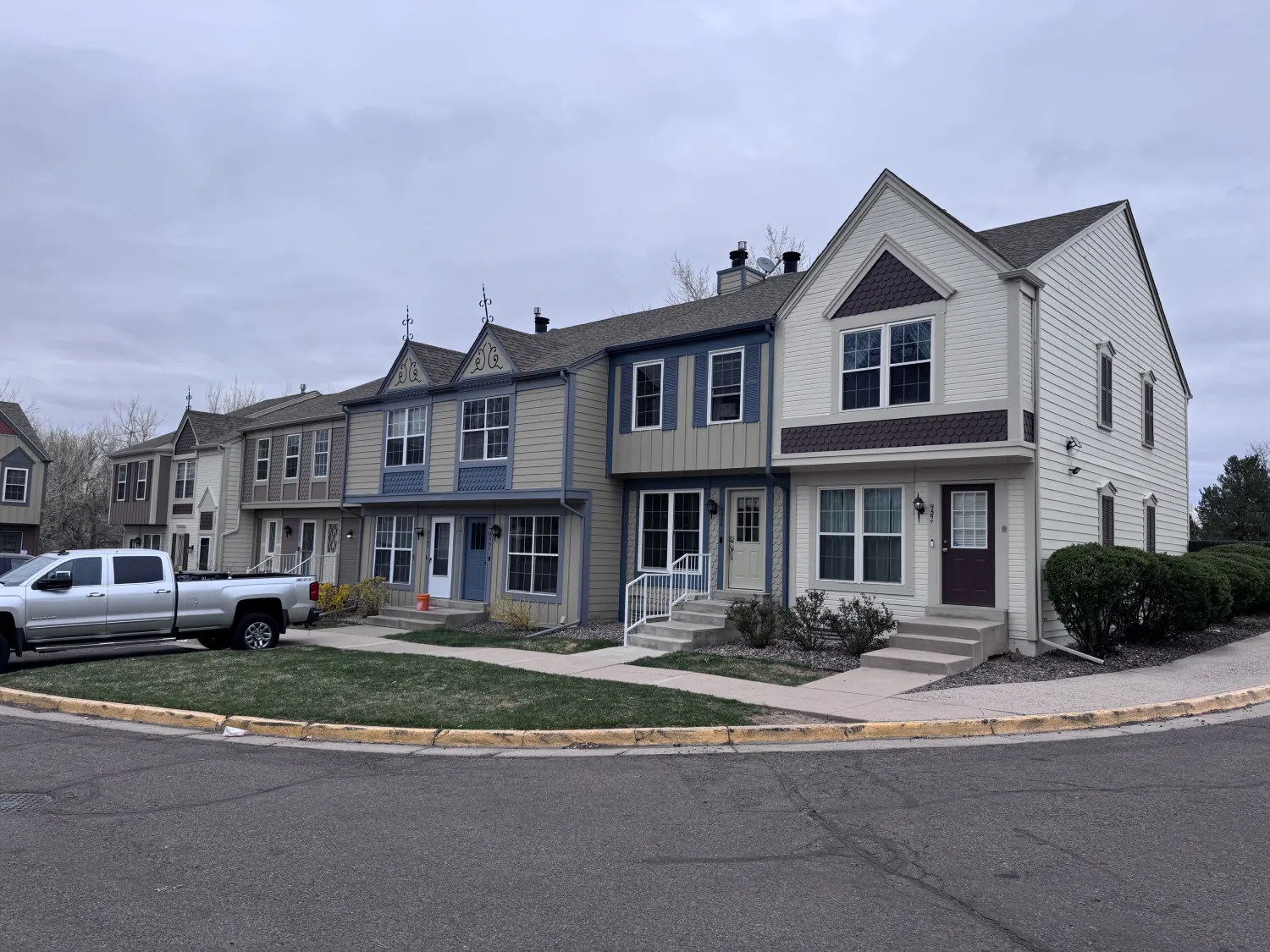 hoa-34 Row of suburban townhouses with parked vehicles and cloudy sky, viewed from a street corner.