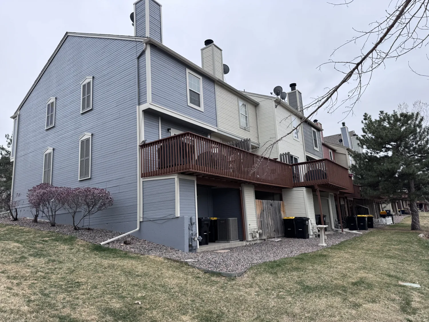 hoa-35 Two-story townhouses with wood balconies, gray siding, and several trash bins on a cloudy day.