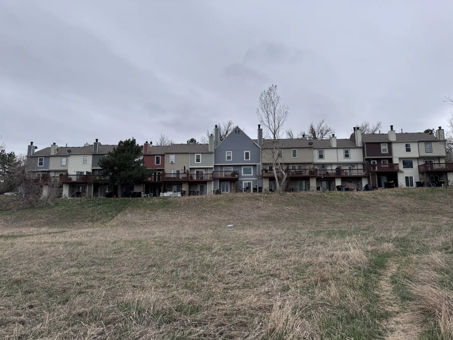 hoa-37 Row of townhouses with decks, seen from a grassy field under an overcast sky.