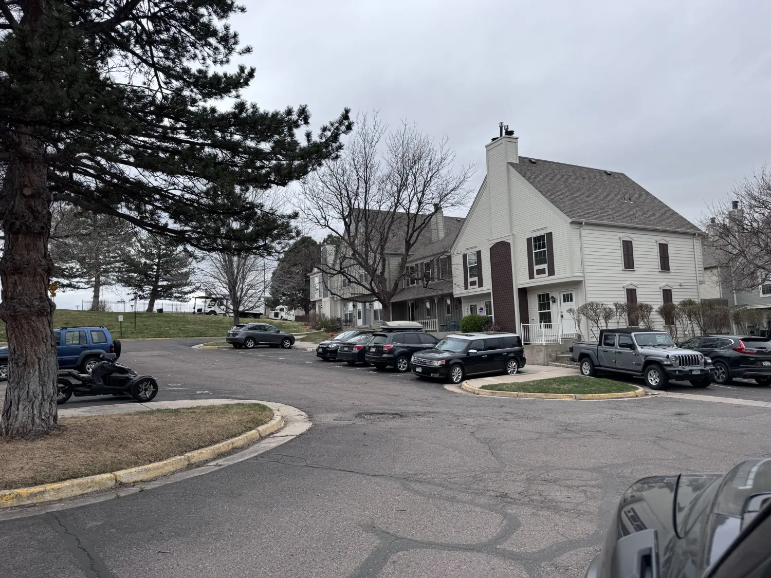 hoa-39 A small parking lot with several cars parked near a two-story white building on a cloudy day.