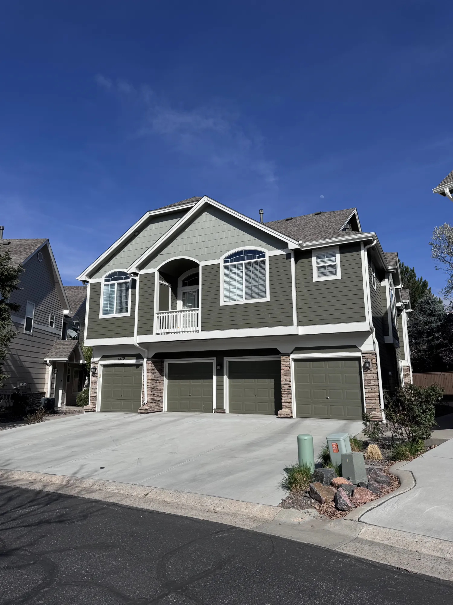 Two-story green house with four garage doors and a small balcony, under a clear blue sky.