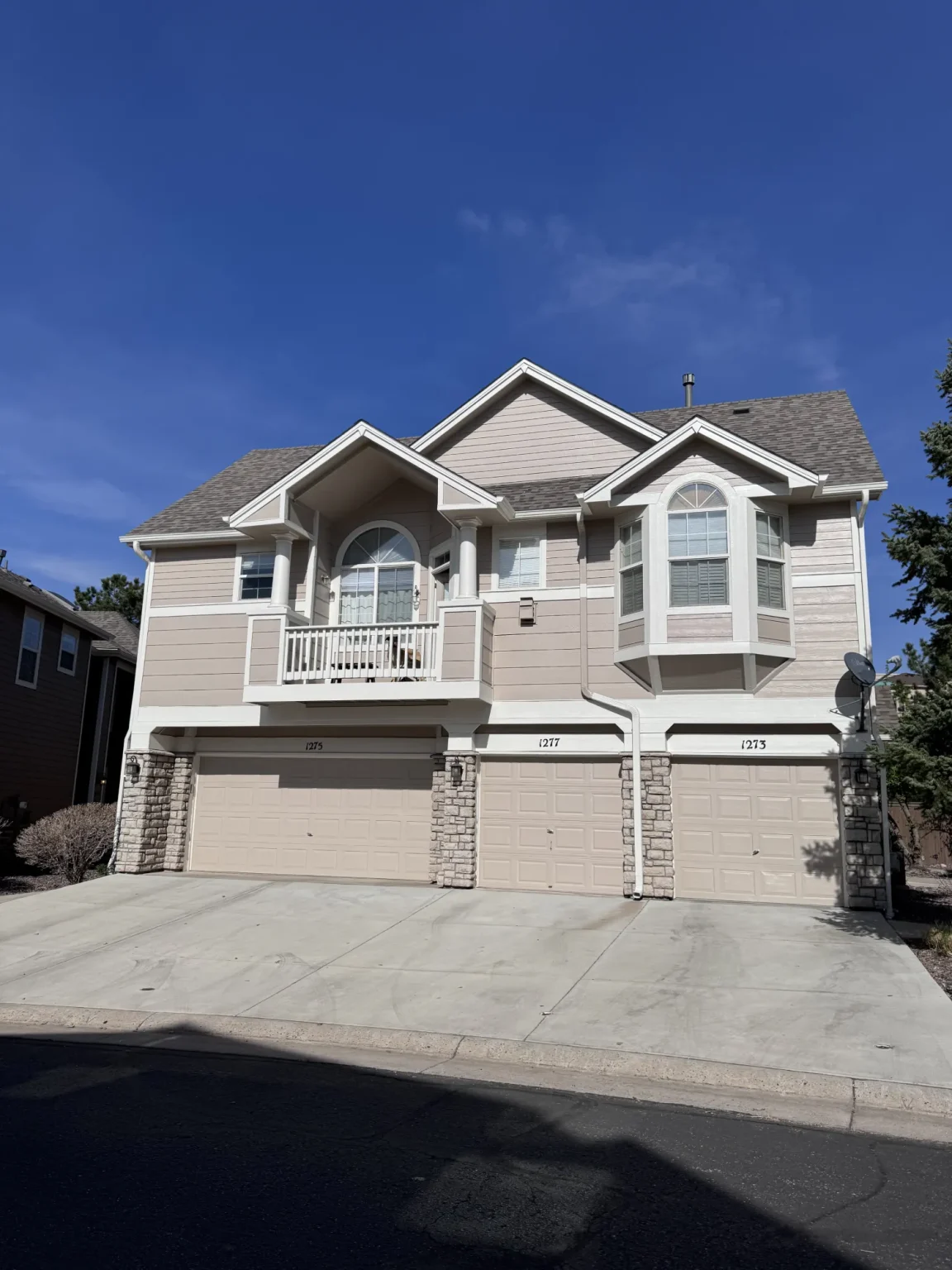 hoa-43 Beige two-story duplex with three garage doors, small balcony, and arched windows on a sunny day.