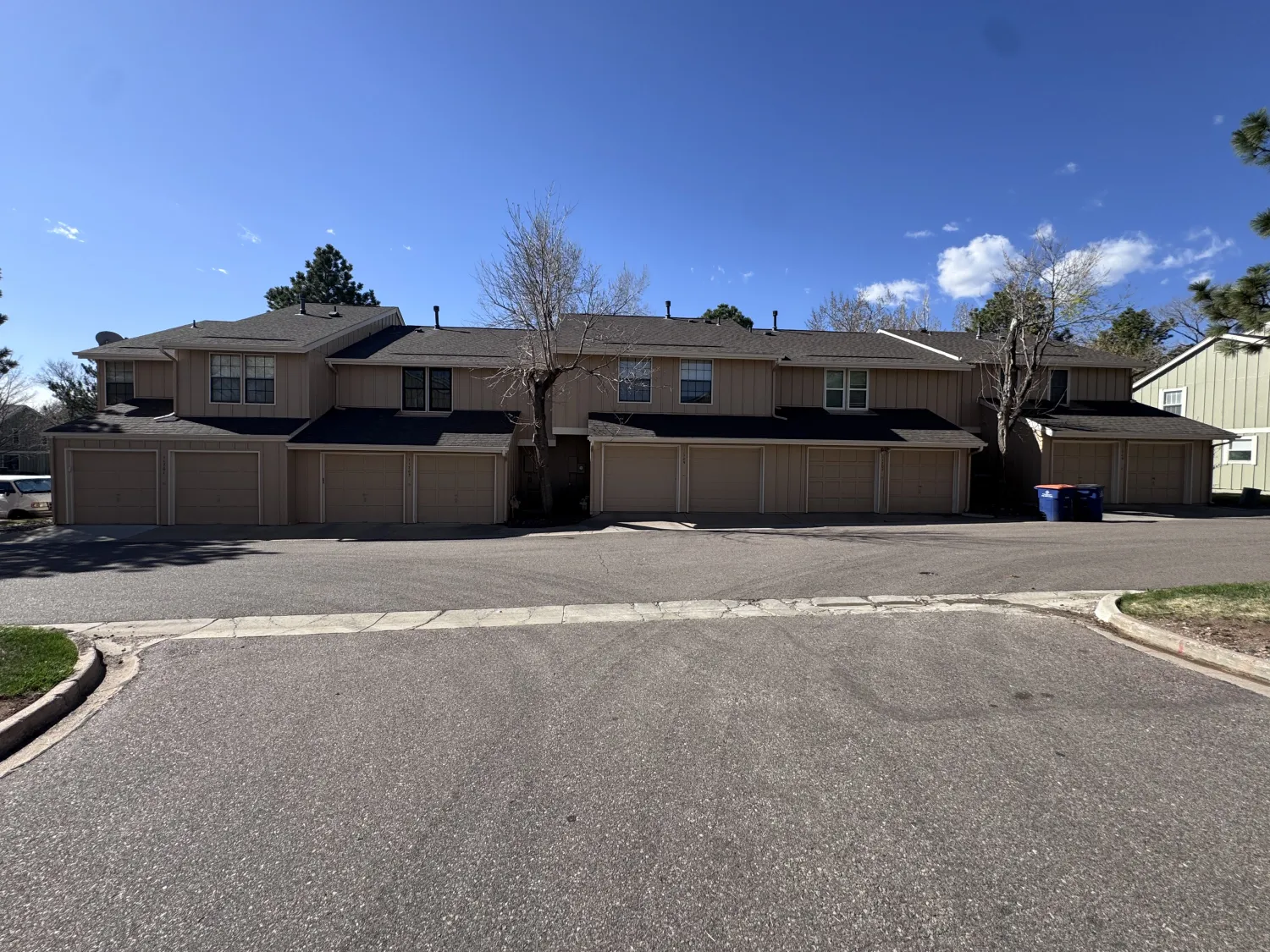 hoa-6 A row of tan townhouses with garages, trees, and a clear blue sky above.