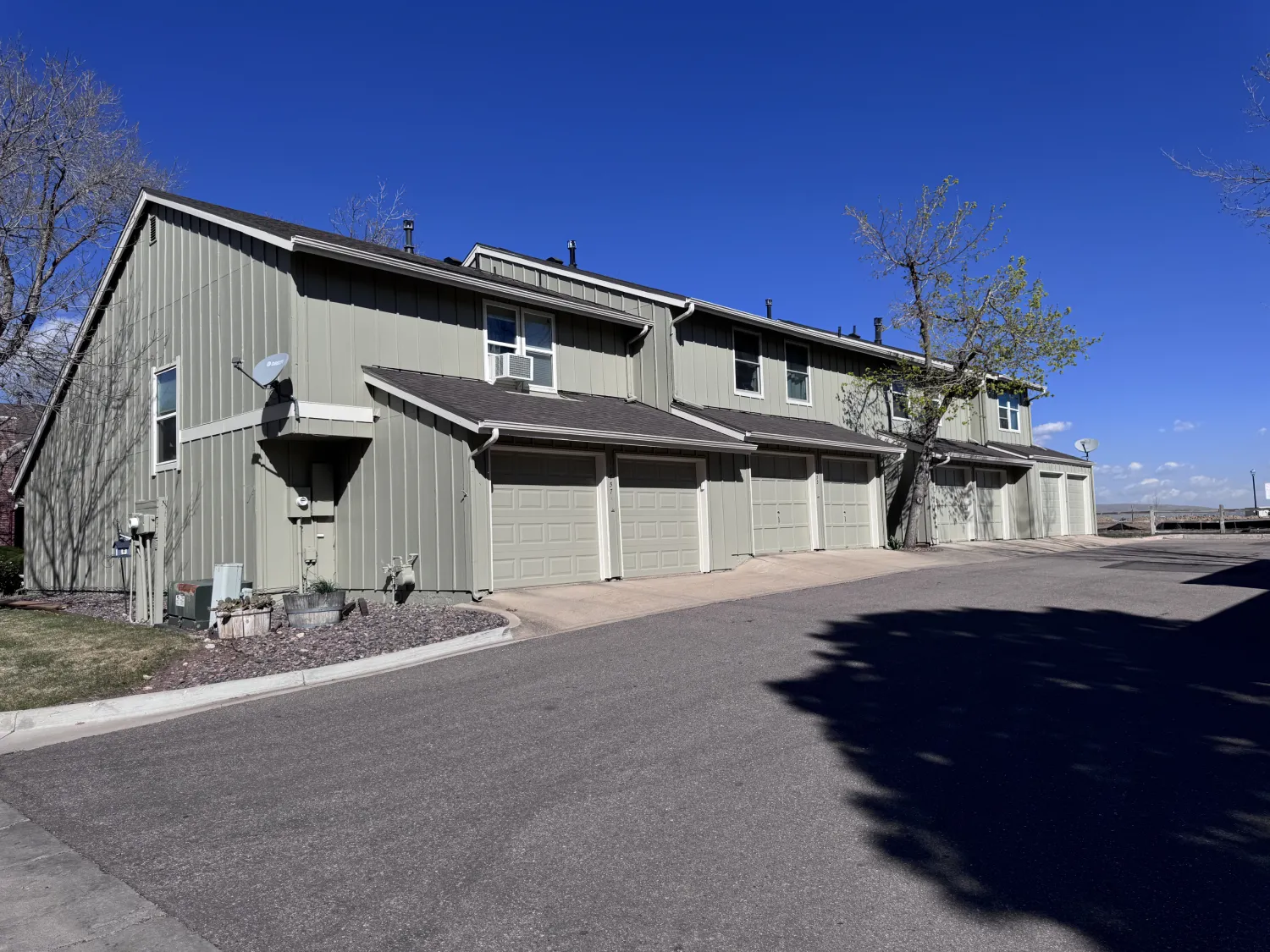 hoa-7 Row of green townhouses with garages under a clear blue sky, trees and driveway in front.