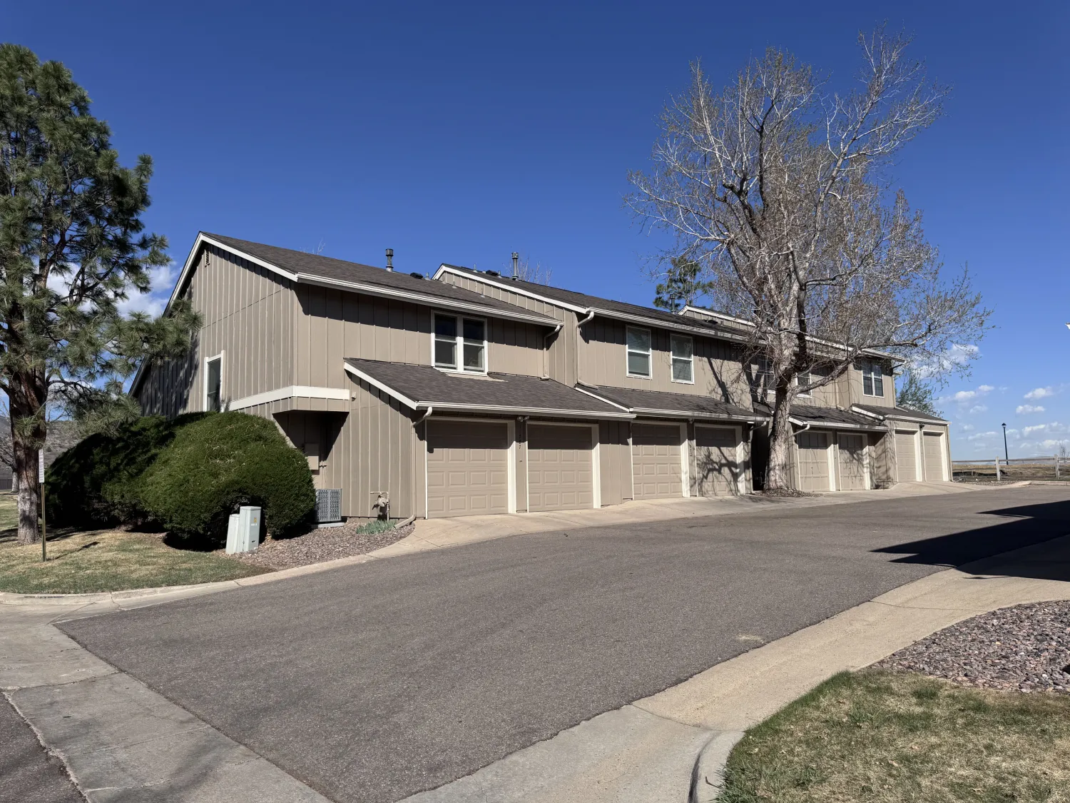 hoa-9 Two-story brown townhouses with garages, leafless tree, and clear blue sky on a sunny day.