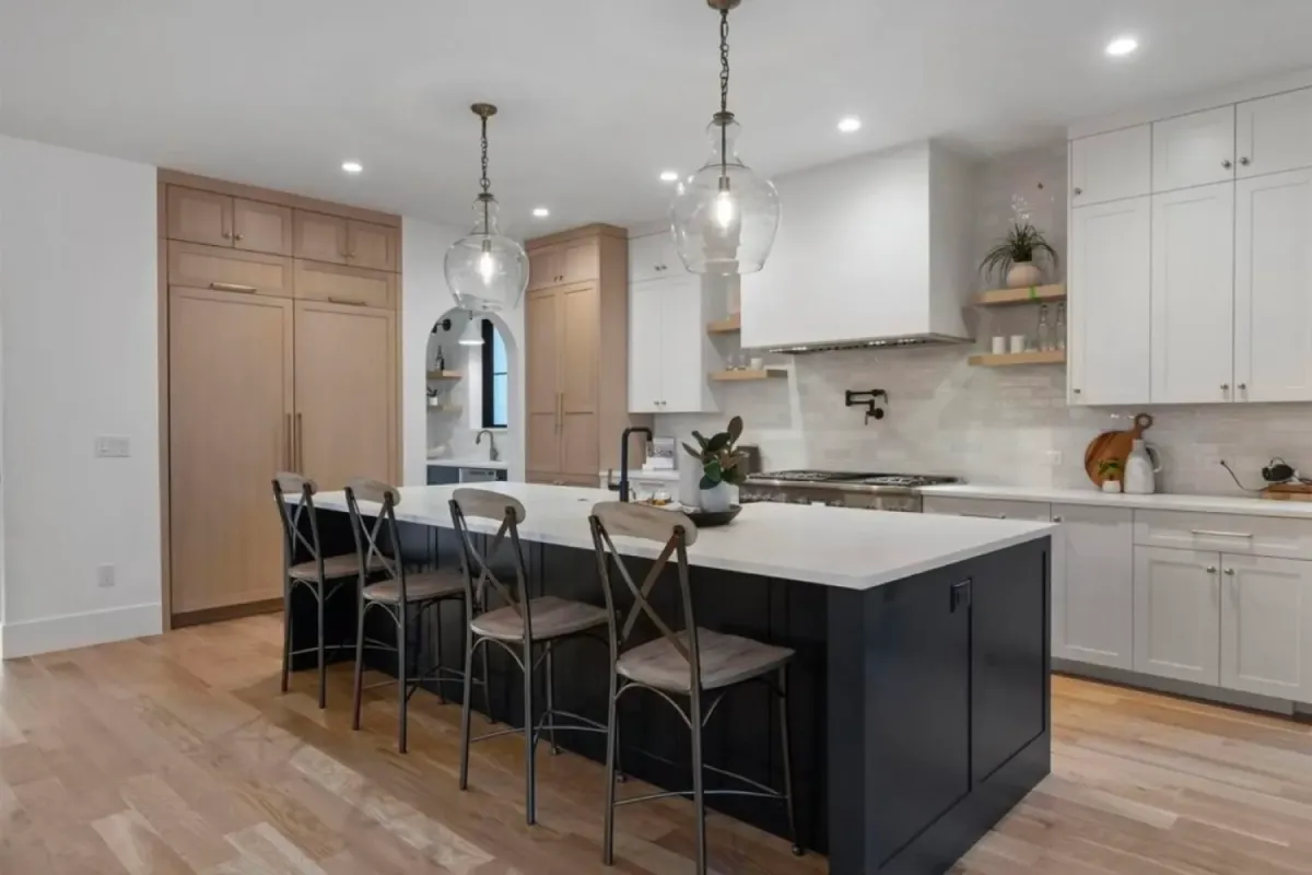 Modern kitchen with island seating, pendant lights, white cabinets, and light wood floors.