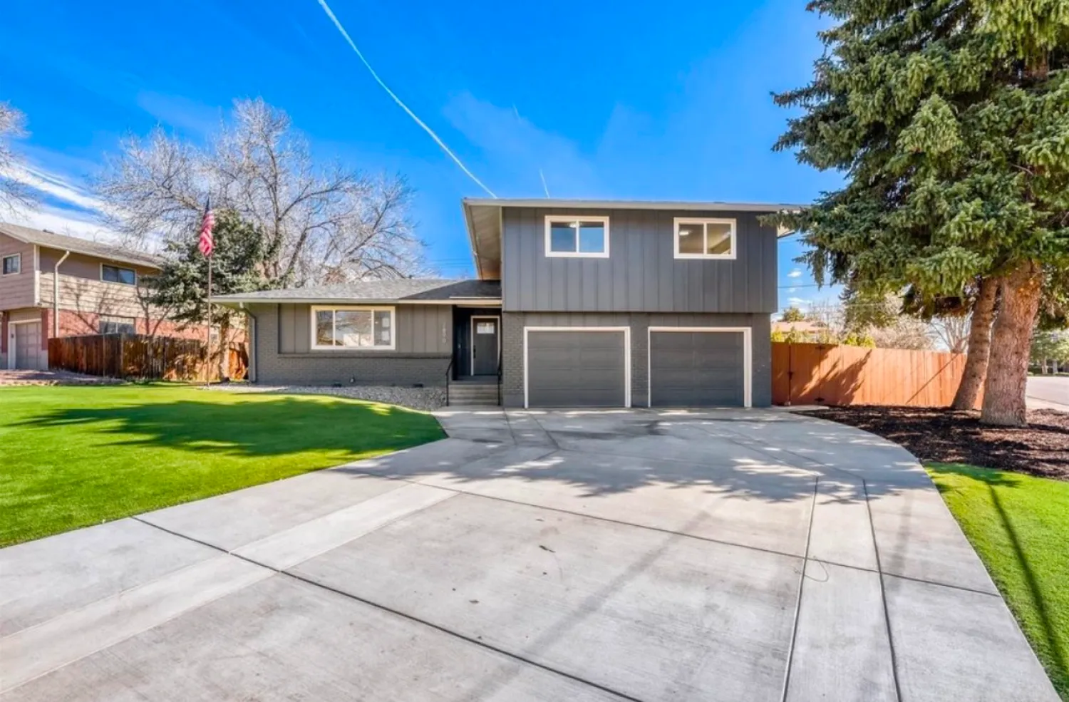 residential-exterior-1 Gray two-story house with double garage, wide driveway, green lawn, and clear blue sky.