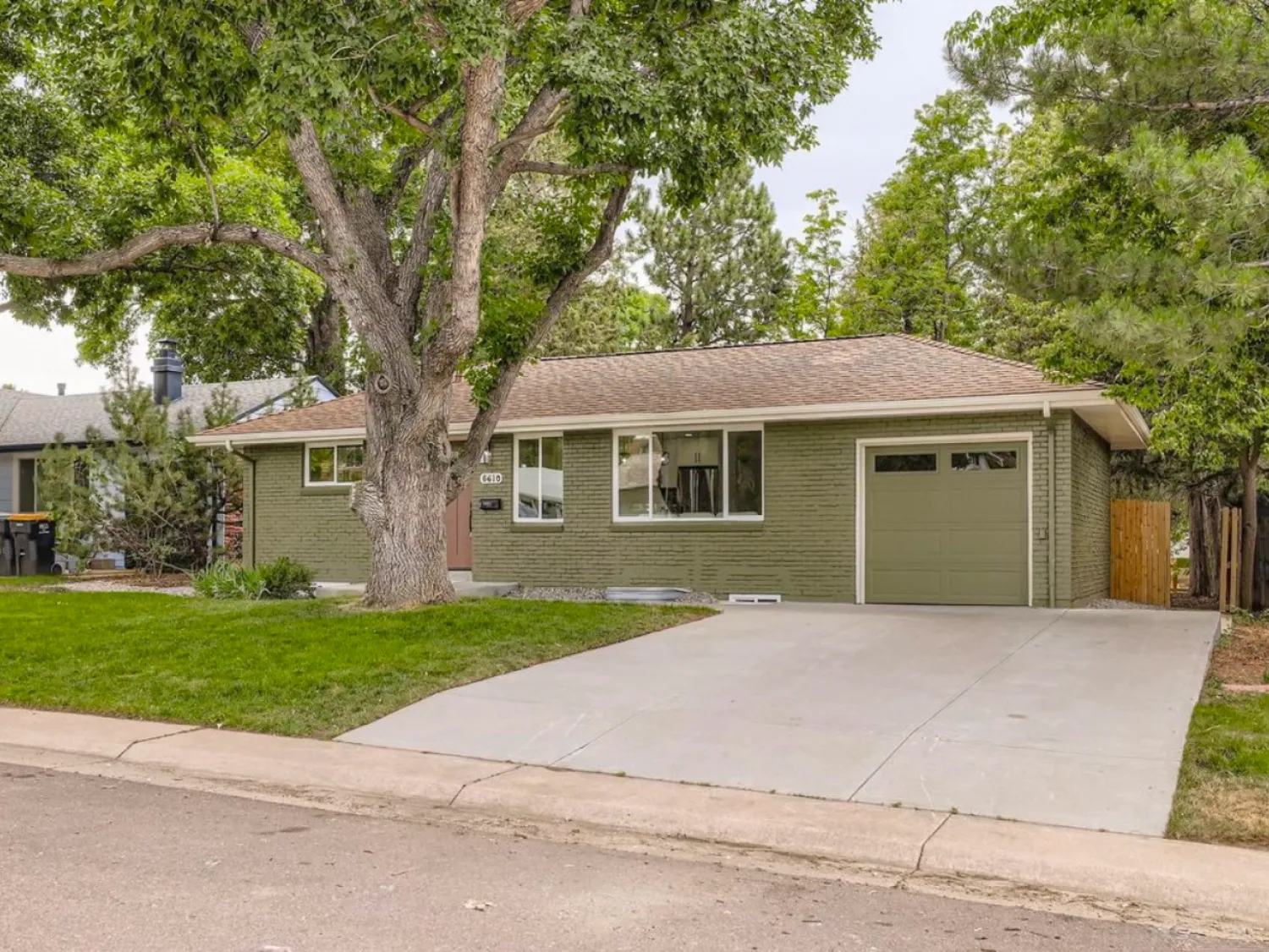 residential-exterior-11 Single-story green house with a large tree, front lawn, and attached garage in a suburban neighborhood.