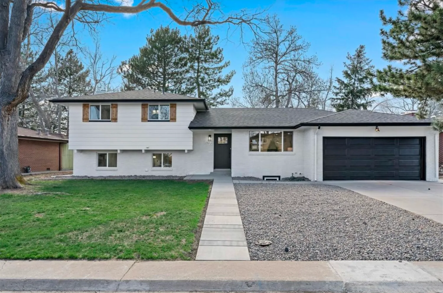 residential-exterior-13 A split-level house with white siding, black garage door, gravel yard, and a sidewalk leading to the front door.