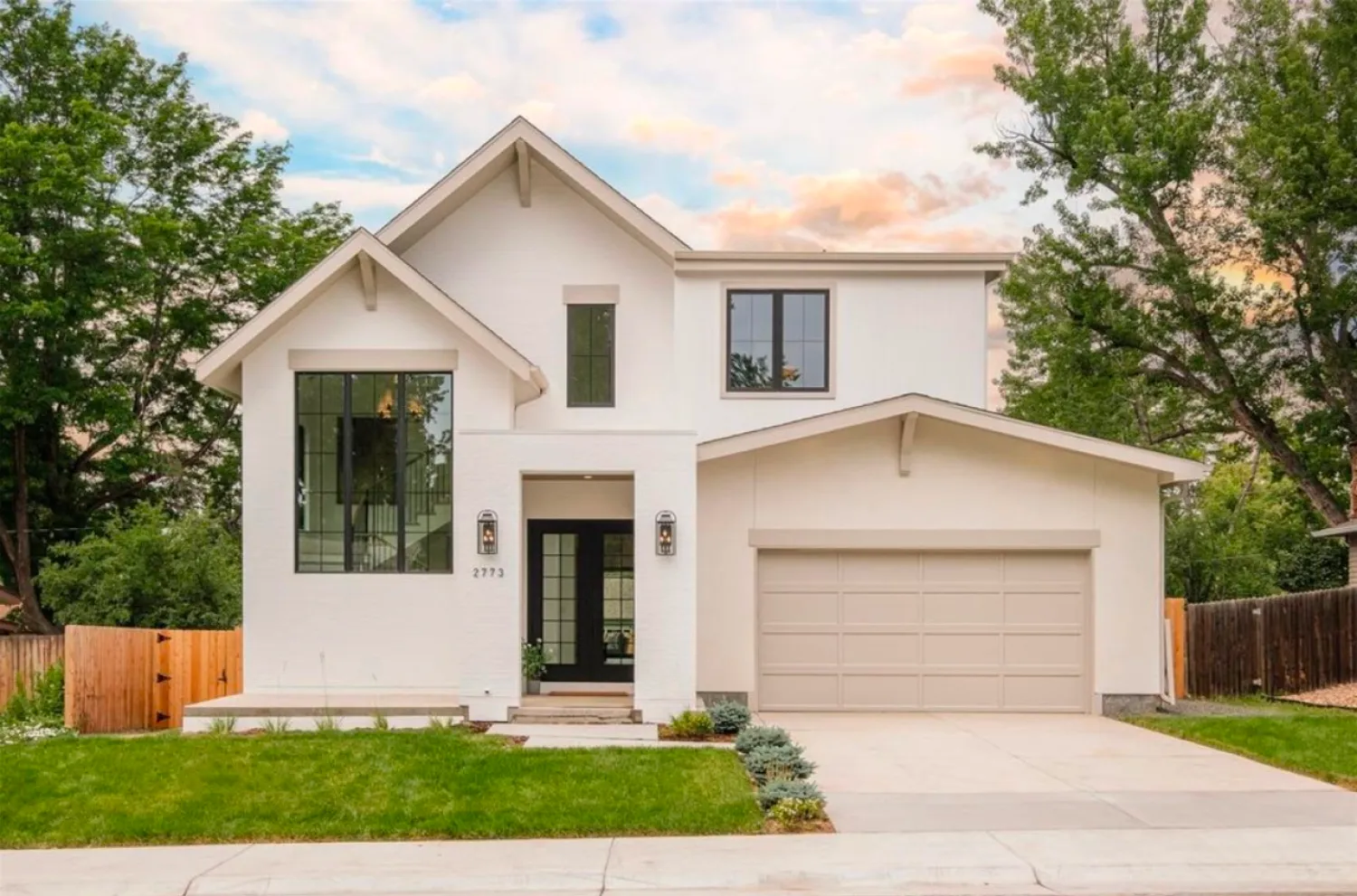 residential-exterior-15 Modern two-story white house with large windows, front porch, and attached two-car garage at sunset.