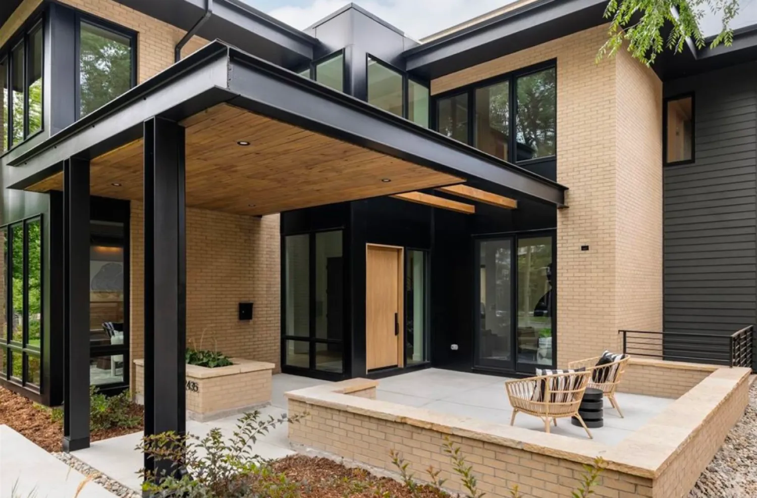 residential-exterior-17 Modern house with large windows, light brick walls, black trim, and a covered entry patio with chairs.