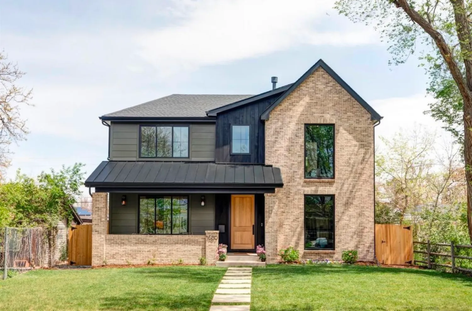 residential-exterior-18 Modern two-story house with brick and dark siding, large windows, wooden door, and a green lawn.