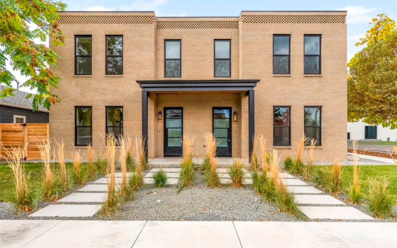 residential-exterior-19 Modern tan brick duplex with large windows, black trim, and landscaped front yard with tall grasses.
