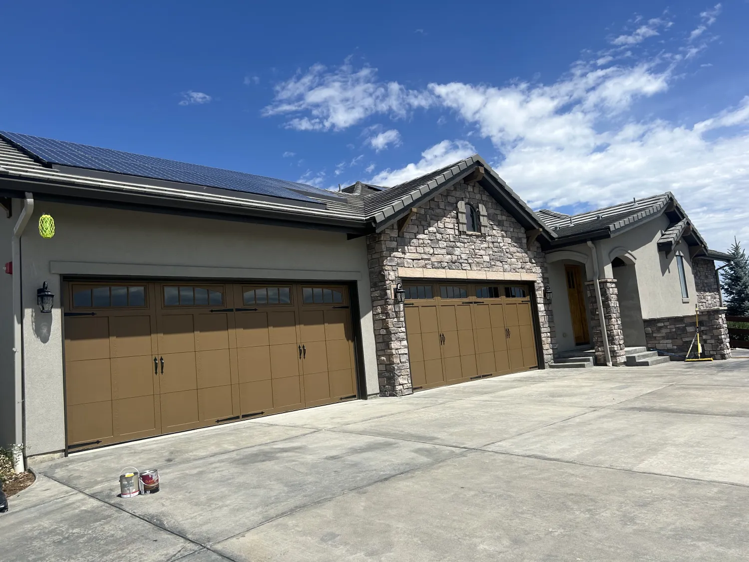 residential-exterior-21 Large house with three brown garage doors, stone accents, and a clear blue sky overhead. Two paint cans on driveway.