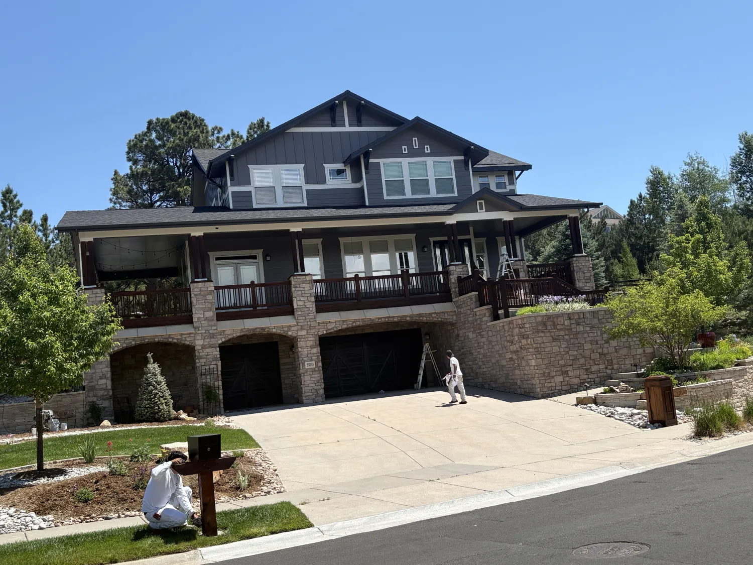 residential-exterior-22 Two people in white coveralls paint a mailbox and railing outside a large stone house on a sunny day.