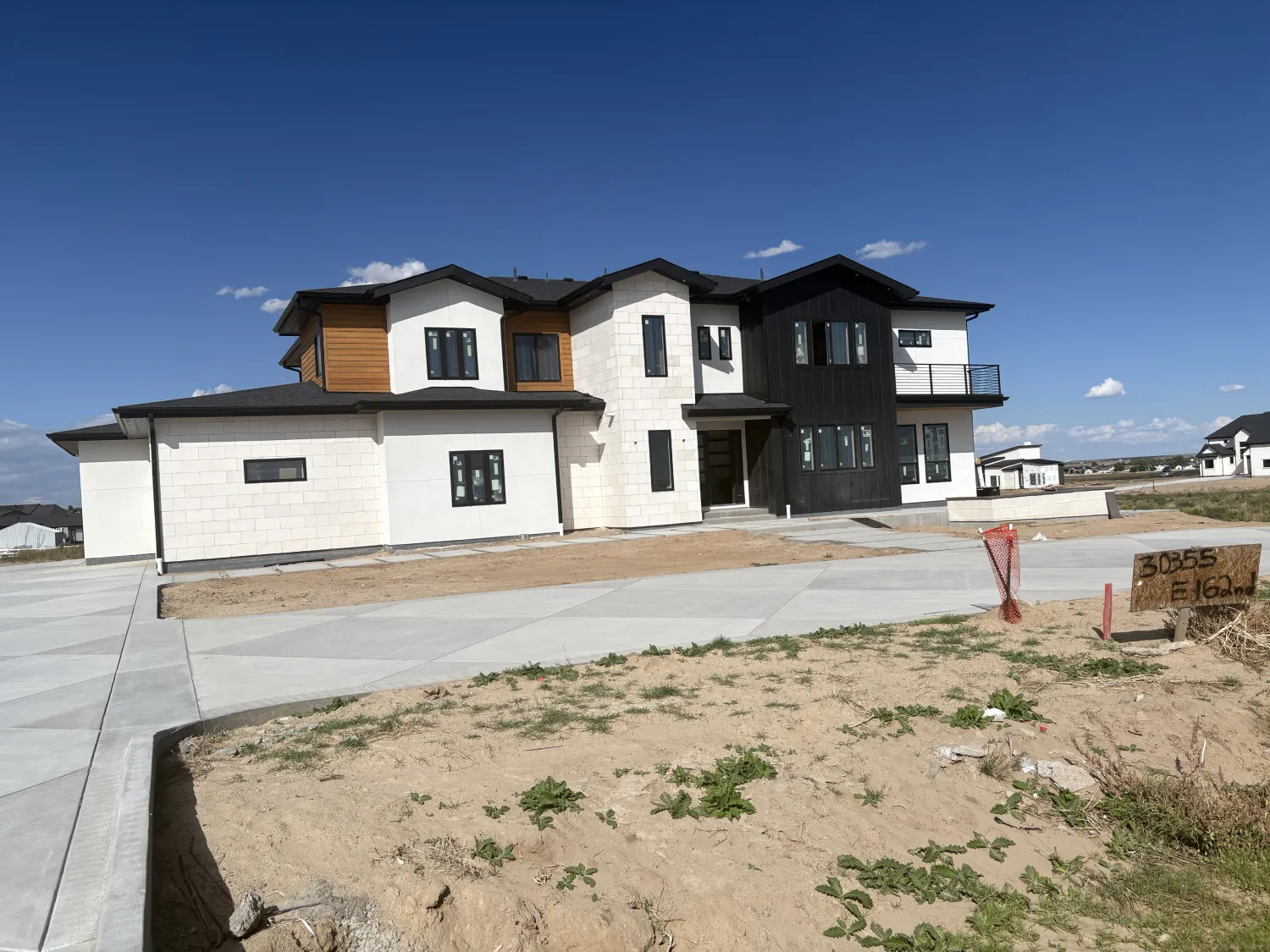 residential-exterior-23 Modern two-story house with white and black exterior, large driveway, and unfinished yard under blue sky.