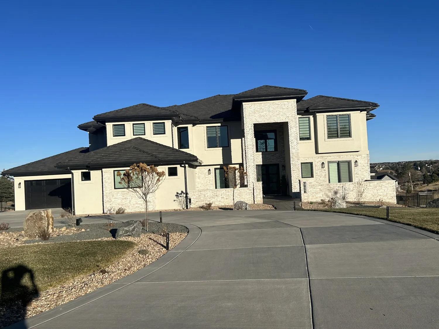 residential-exterior-25 Modern two-story house with stone accents, black roof, and a large curved driveway on a clear day.