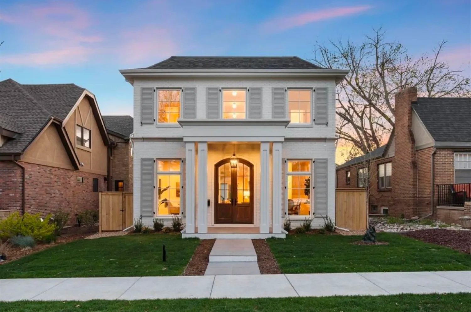 residential-exterior-7 Two-story white house with large windows, wooden front door, and a manicured lawn at sunset.