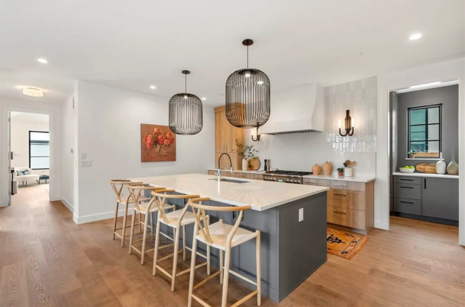 residential-interior-1 Modern kitchen with island seating, pendant lights, wood floors, and adjacent pantry area.
