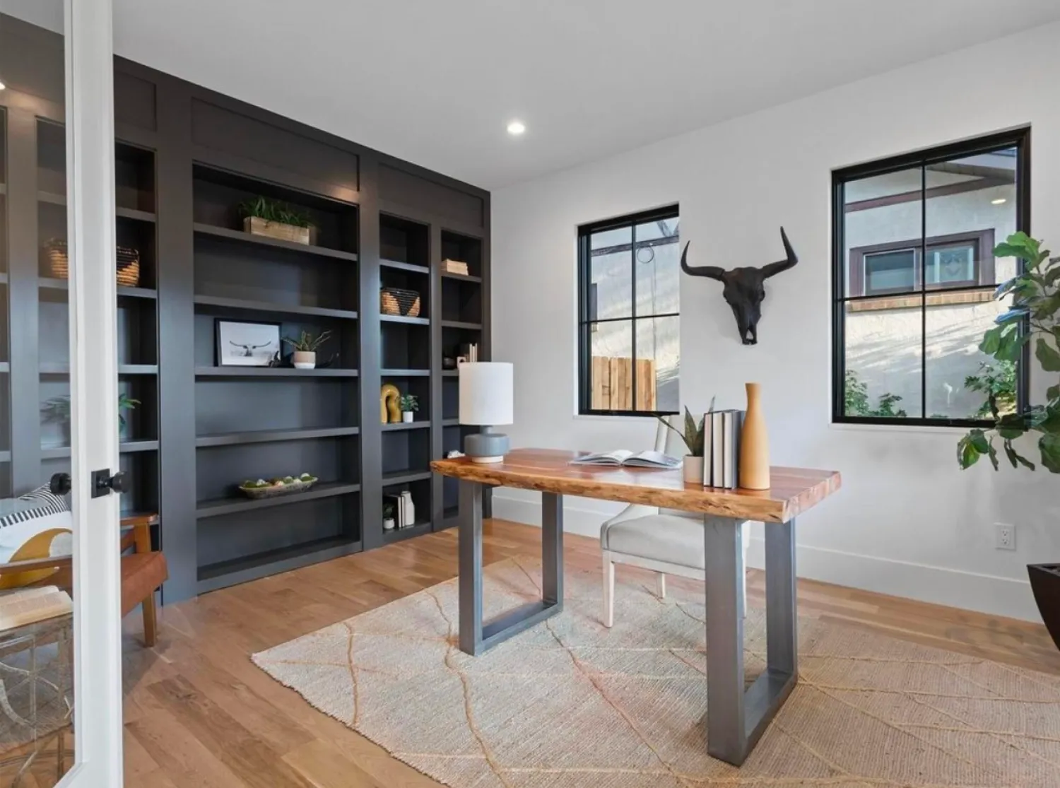 residential-interior-10 Modern home office with wood desk, built-in shelves, bull skull wall decor, and large windows.
